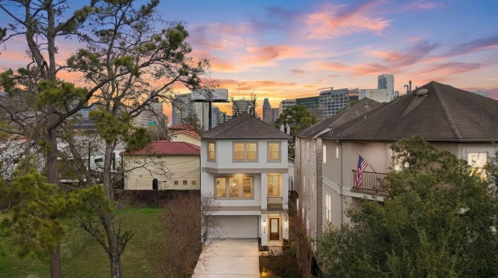 A three-story home among trees with the Houston skyline at sunset